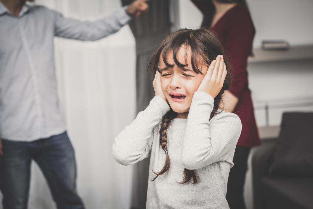 Weinendes Kind, das sich vor streitenden Eltern die Ohren zuhält